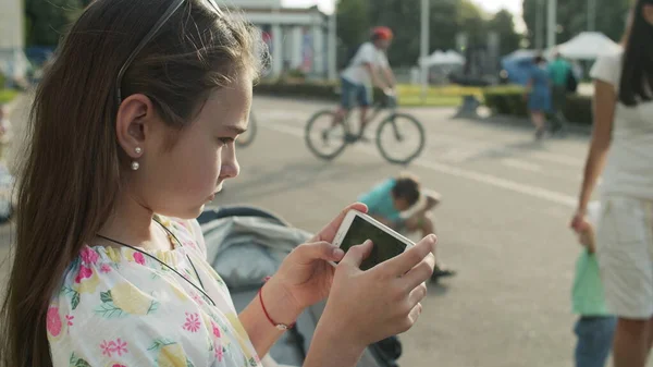Komoly lány, aki mobilon játszik a parkban. Aranyos lány telefonál odakint. — Stock Fotó