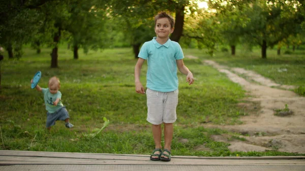 Lächelnder Teenager, der draußen tanzt. Kleineres Kind trägt Frisbee-Teller draußen — Stockfoto
