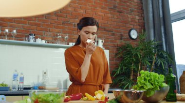 Girl preparing vegetable salad in kitchen. Woman smelling fresh onion bulb.