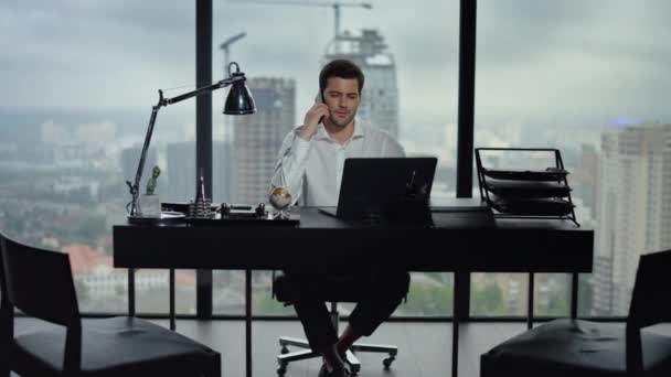 Uomo d'affari che parla su smartphone sul posto di lavoro. Uomo seduto a tavola con computer portatile — Video Stock