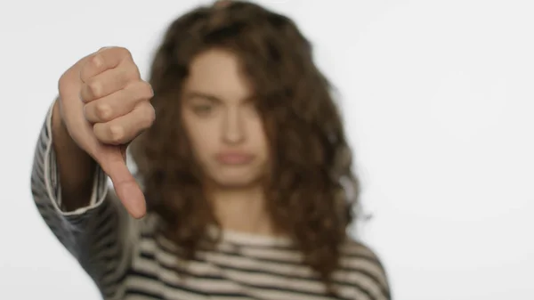 Smutna dziewczyna pokazuje kciuki w studio. Zdenerwowana kobieta pokazuje niechęć do znaku strony — Zdjęcie stockowe