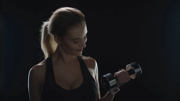 Fitness mujer levantamiento de pesas mancuerna y mirando a la cámara sobre fondo negro — Foto de Stock