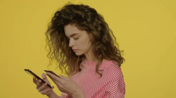 젊은 여성이 스마트폰으로 돈 앱을 사용하여 노란색 스튜디오에서 은행 카드를 지불하는 모습 — 스톡 사진
