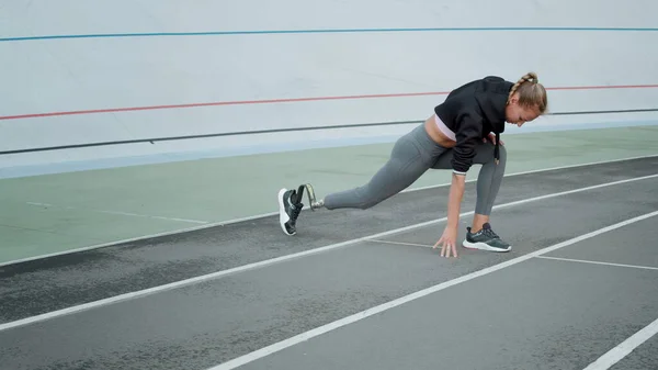 Handicapped fit girl stretching legs at stadium. Athlete warming at stadium