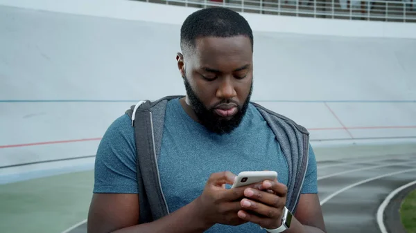 Sportler beim SMS-Schreiben auf dem Smartphone auf der Strecke. Guy liest gute Nachrichten auf dem Handy — Stockfoto