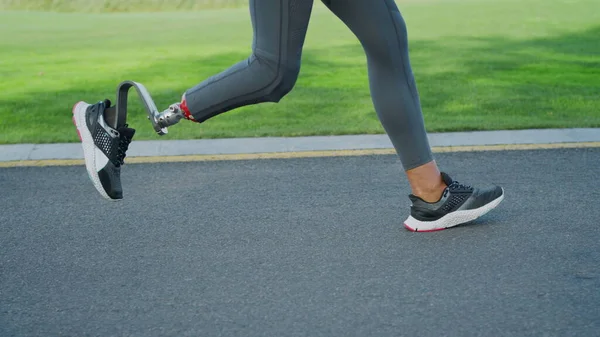 Mujer con una pierna protésica corriendo por la carretera. Mujer deportista entrenando al aire libre —  Fotos de Stock