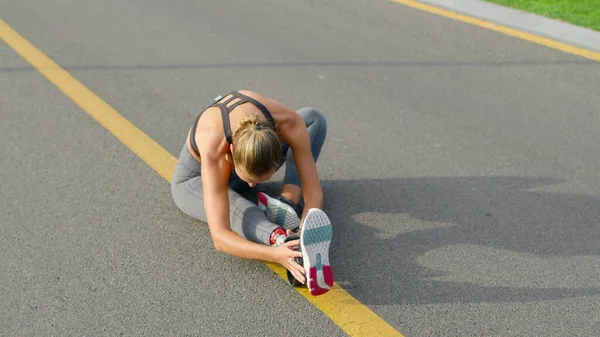 Chica discapacitada estirando las piernas en la carretera. Calentamiento del corredor después del entrenamiento —  Fotos de Stock