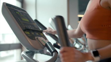 Spor salonunda eliptik antrenör kullanan kimliği belirsiz formda bir kız. Kulüpte kadın vücudu ısınıyor.