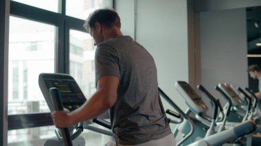Formda adam spor kulübünde ısınıyor. Spor salonunda eliptik antrenör kullanan erkek sporcu