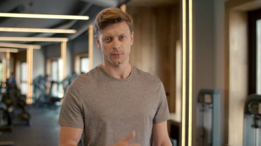 Yakışıklı fitnessman spor kulübünde baş parmağını gösteriyor. Sporcu spor salonunda duruyor..