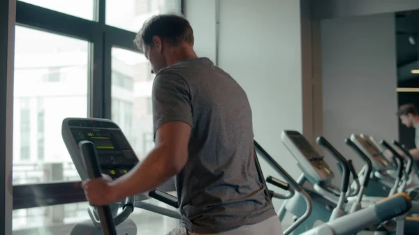 Fit man warming up in sport club. Male athlete using elliptical trainer at gym