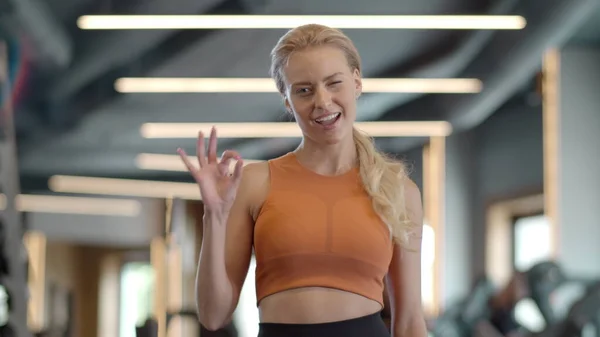 Zabawna kobieta fitness pokazuje znak ok na siłowni. Sportowiec stojący w klubie sportowym — Zdjęcie stockowe