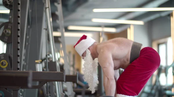 Aktif fitness adamı spor salonunda kaldırma yapıyor. Noel Baba kostümlü adam antrenman yapıyor. — Stok fotoğraf