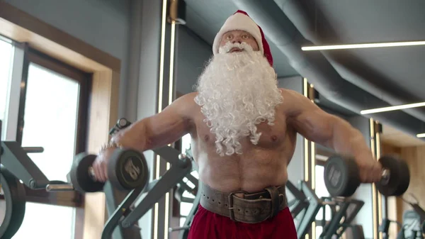 Babbo Natale si allena nel club sportivo. Sexy Santa facendo manubri altalene in palestra. — Foto Stock