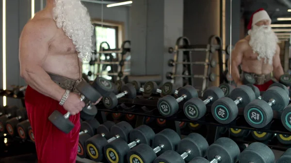 Babbo Natale forte che fa riccioli di bicipiti in palestra. Allenamento sportivo nel club sportivo — Foto Stock