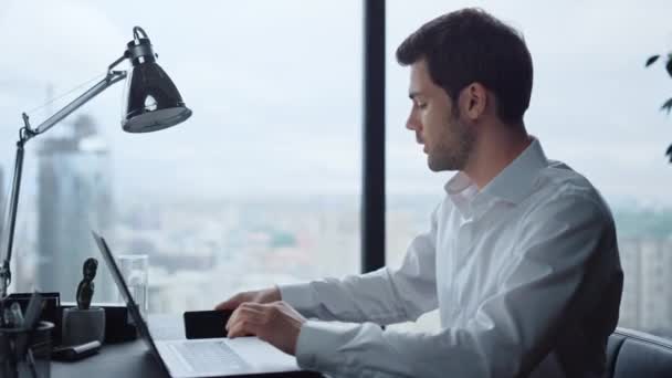 Empresario trabajando en laptop en el lugar de trabajo. Gerente mirando la pantalla del teléfono inteligente — Vídeos de Stock