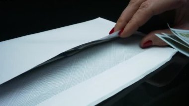 Tanınmayan bir kadın Amerikan dolarlarını zarfa koyuyor.