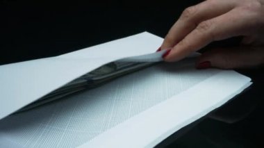 İş kadını elleri 100 dolarlık banknotları zarfa koyuyor.