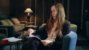 Hüzünlü iş kadını, akşam otel lobisinde belgeleri kontrol ediyor.