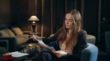 Gece otel lobisinde belgelerle çalışan ciddi bir iş kadını.