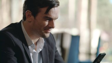 Gülümseyen işadamı restoranda akıllı telefondan iyi haberler okuyor.