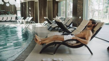 Yakışıklı adam yüzme havuzunun yanında dinleniyor. Suya bakan zengin bir adam.