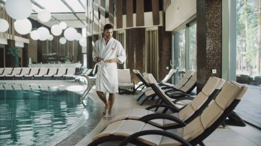 Otelde su havuzunun yanında yürüyen yakışıklı bir adam. Formda bir adam spa havuzunun yanında dinleniyor..