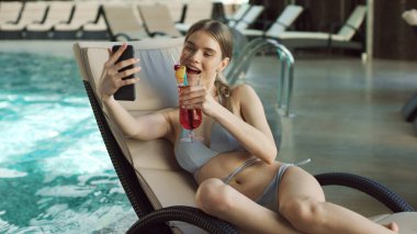 Havuz başında video görüşmesi yapan seksi kadın. Flört eden kız kokteyl içiyor..