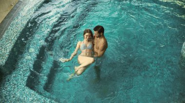 Havuzda birlikte banyo yapan bir çift. Yukarıda havuzda rahatlayan genç bir aile.