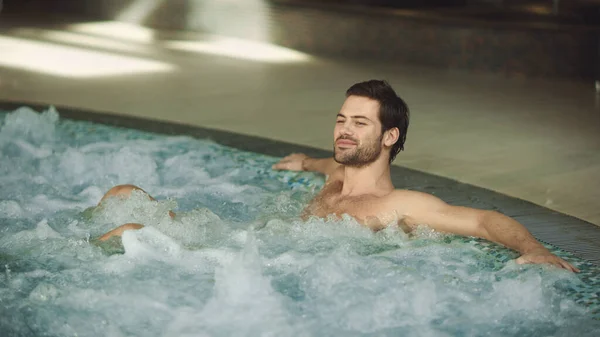 Aantrekkelijke man rustend bubbelbad binnen. Happy man ontspannen in het zwembad. — Stockfoto