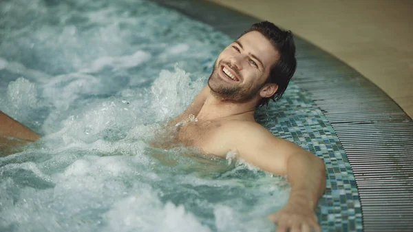 Smiling man relaxing in jacuzzi spa indoor. Sexy guy resting in whirlpool bath — Stock Photo, Image