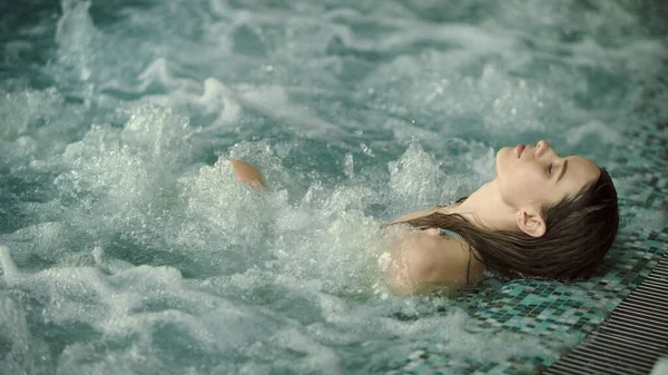 Jovem relaxante na piscina no spa de luxo. Menina bonita tomando banho no jacuzzi — Fotografia de Stock