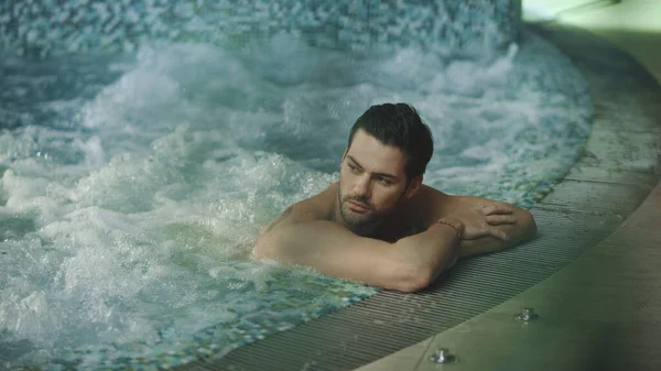 Havuzda spa otelinde dinlenen seksi adam. Kaplıcadaki jakuzide ıslak saçlara dokunan adam.