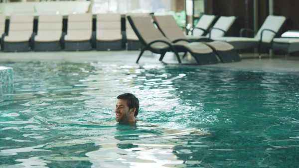 Lächelnder Mann schwimmt im modernen Hotel. Sexy guy baden bei luxus pool indoor. — Stockfoto