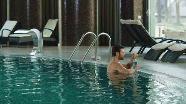 Atractivo hombre bebiendo cóctel en la piscina de lujo. Chico relajándose con alcohol — Foto de Stock