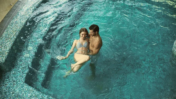 Havuzda birlikte banyo yapan bir çift. Yukarıda havuzda rahatlayan genç bir aile.