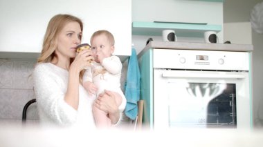 Anne kahve içiyor ve küçük bebeği mutfakta tutuyor. Doğum izni.