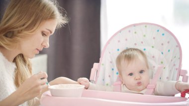 Genç anne bebeği kaşıkla besliyor. Anne besleyen çocuk