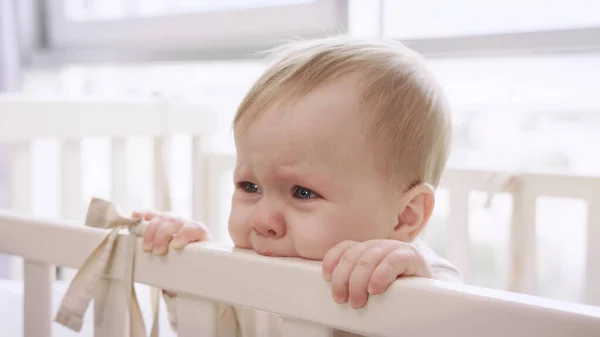 Bebek karyolasını kemiren üzgün kız. Küçük bebek yatakta ağlıyor.