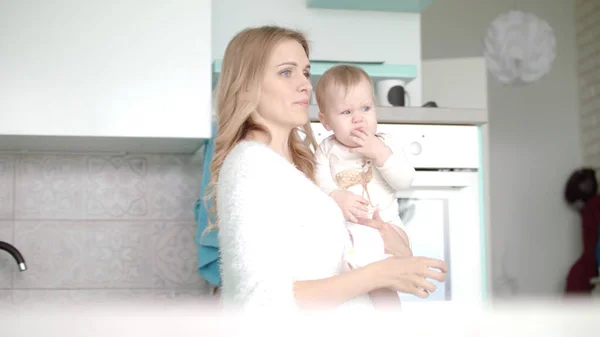 Bebekli anne beyaz mutfağa giriyor. Küçük çocuğu olan güzel bir kadın. — Stok fotoğraf