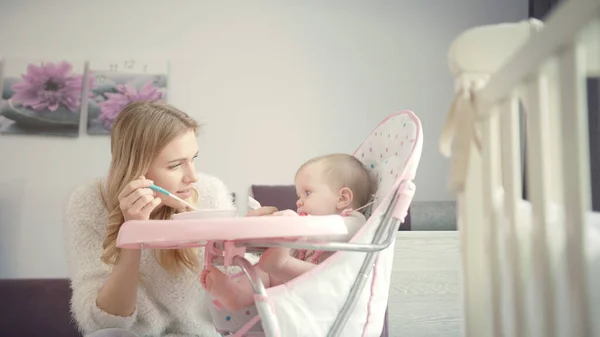 Beautiful mom try feeding baby with porridge. Infant gnawing teethers — Stock Photo, Image