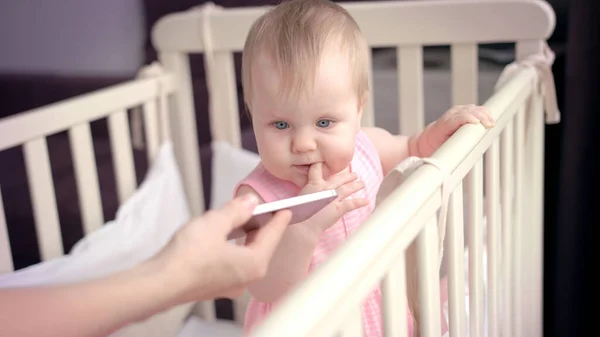 Babymeisje in babybed. Leuke baby uitziende smartphone. Peuter in bed — Stockfoto