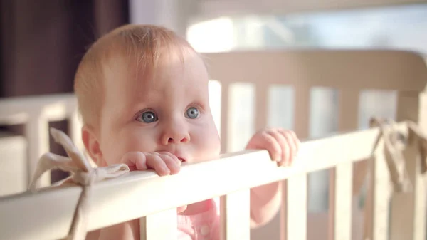 De baby staat thuis in bed. Portret van een meisje in een wieg. Kleine oogjes — Stockfoto