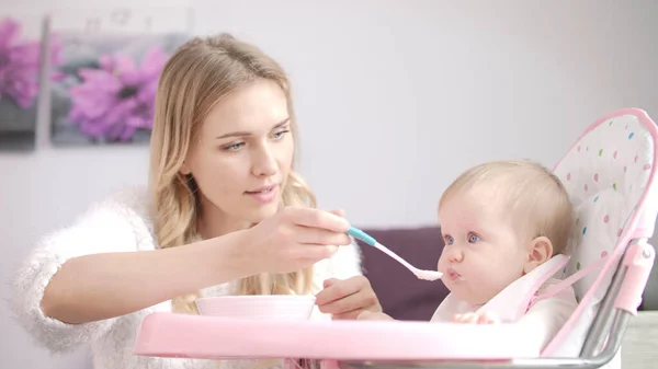 Mutter füttert Kind im Babystuhl. Frau füttert Baby mit Haferbrei — Stockfoto