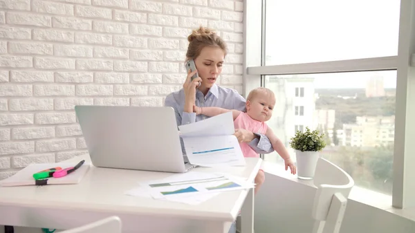 Business mother with baby talking mobile phone. Woman working with child