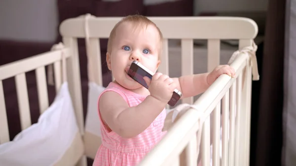 Niedliches Baby isst Handy. Smartes Mobiltelefon im Kinderbett — Stockfoto