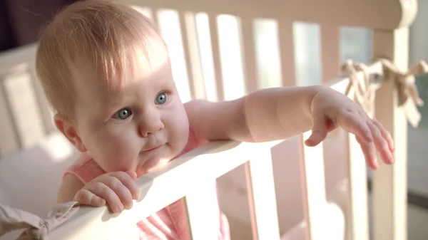 Liebenswertes Baby reicht Hand in Hand Kinderbett. Kleines Kind mit interessantem Gesicht — Stockfoto