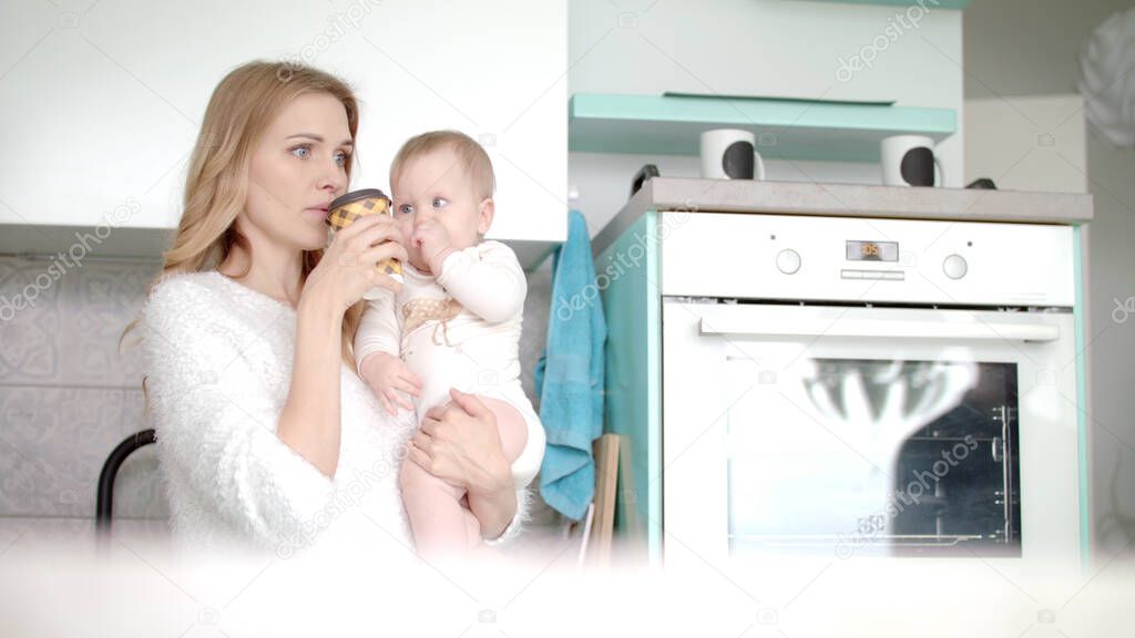 Mother drinking coffee and hold little baby on kitchen. Maternity leave