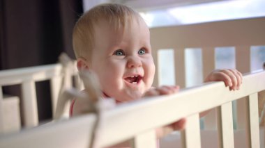 Beşikteki neşeli çocuk. Gülümseyen bebek evde yatakta duruyor.
