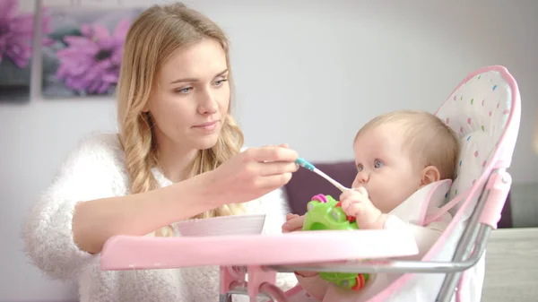 Παιδί με παιχνίδι τρώει πολτοποιημένα τρόφιμα από μπολ μωρό. Γυναίκα σίτιση μωρό στην καρέκλα — Φωτογραφία Αρχείου
